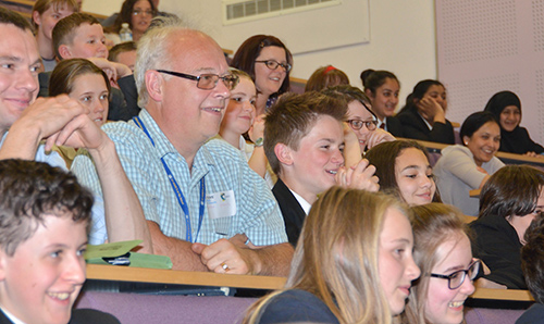 Academics and school students observing something off camera in a lecture theatre