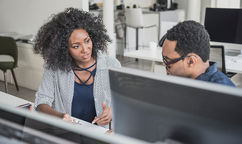 Man and woman discussing contents of mobile phone screen at desk