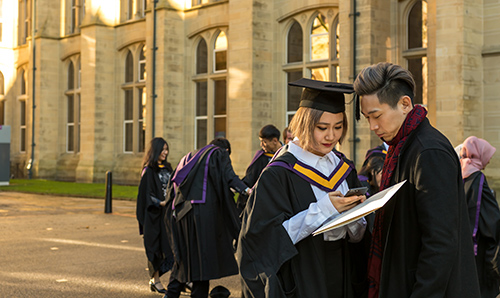 A newly graduated couple stand in graduation gowns outside Whitworth Hall